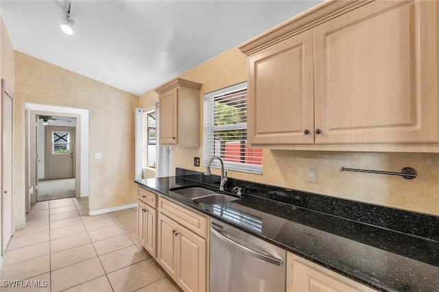 kitchen featuring dark stone countertops, light brown cabinetry, sink, light tile patterned floors, and stainless steel dishwasher