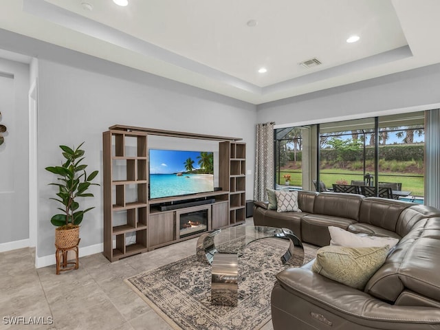 living area featuring visible vents, a raised ceiling, baseboards, and a glass covered fireplace