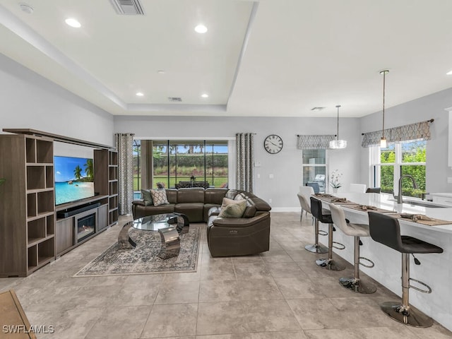 living area with recessed lighting, visible vents, a raised ceiling, and baseboards