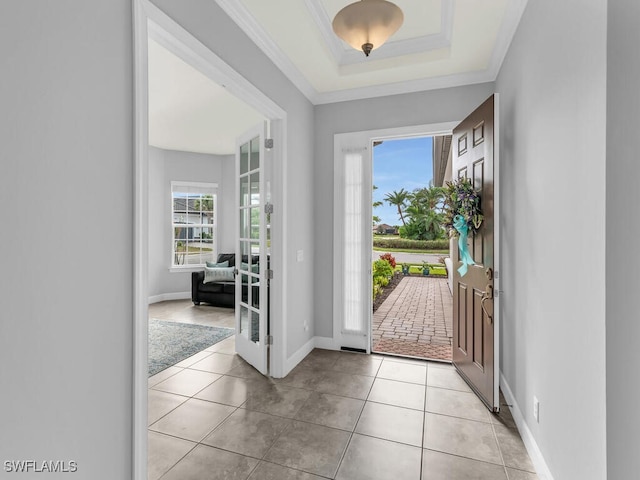 foyer entrance with a tray ceiling, light tile patterned flooring, and crown molding