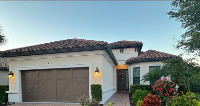 mediterranean / spanish-style house featuring driveway, an attached garage, a tiled roof, and stucco siding