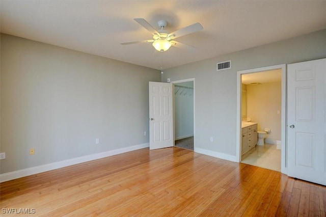 unfurnished bedroom featuring ceiling fan, light hardwood / wood-style floors, a spacious closet, connected bathroom, and a closet