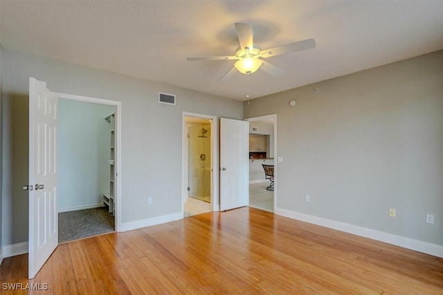 unfurnished bedroom with ceiling fan, connected bathroom, a walk in closet, and hardwood / wood-style floors