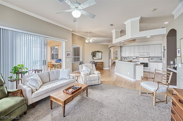 living room featuring ceiling fan, sink, ornamental molding, and light wood-type flooring