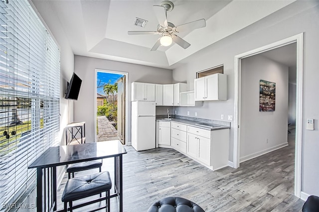 kitchen with light wood-type flooring, white cabinetry, a raised ceiling, and white fridge