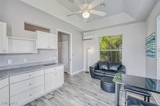 kitchen with white cabinetry, an AC wall unit, a raised ceiling, light hardwood / wood-style flooring, and ceiling fan