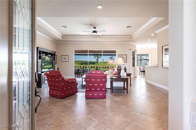 living room with a ceiling fan, baseboards, visible vents, ornamental molding, and a raised ceiling