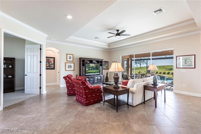 living room featuring a raised ceiling, baseboards, arched walkways, and ornamental molding