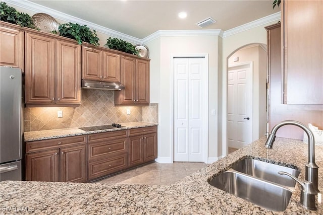 kitchen with freestanding refrigerator, ornamental molding, decorative backsplash, a sink, and under cabinet range hood