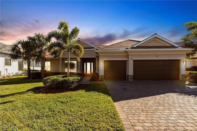 view of front of house featuring decorative driveway, a yard, a garage, and stucco siding