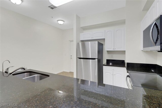 kitchen with appliances with stainless steel finishes, dark stone countertops, white cabinets, and sink