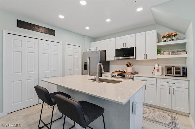 kitchen featuring a kitchen island with sink, sink, stainless steel appliances, and white cabinetry