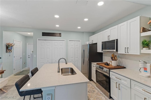 kitchen with a kitchen bar, sink, appliances with stainless steel finishes, an island with sink, and light stone counters