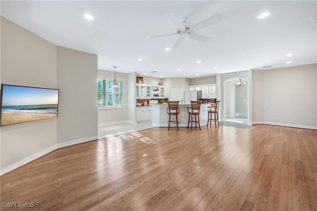 unfurnished living room featuring recessed lighting, ceiling fan with notable chandelier, light wood-type flooring, and baseboards