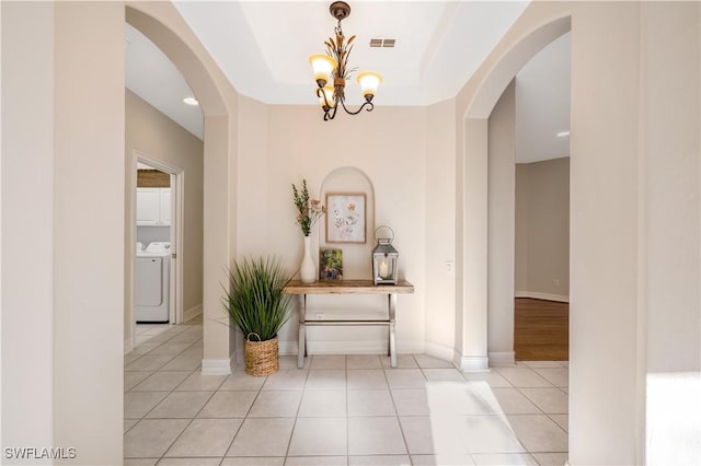 hallway with visible vents, a notable chandelier, washer and clothes dryer, arched walkways, and light tile patterned floors