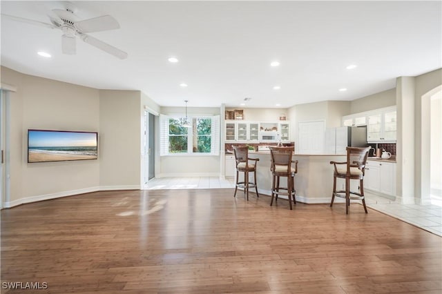 kitchen with light wood finished floors, glass insert cabinets, a breakfast bar, recessed lighting, and white cabinetry