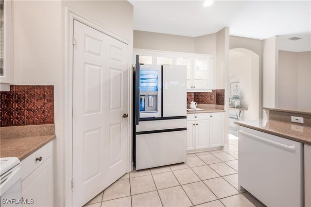 kitchen with backsplash, light tile patterned floors, arched walkways, white appliances, and white cabinetry