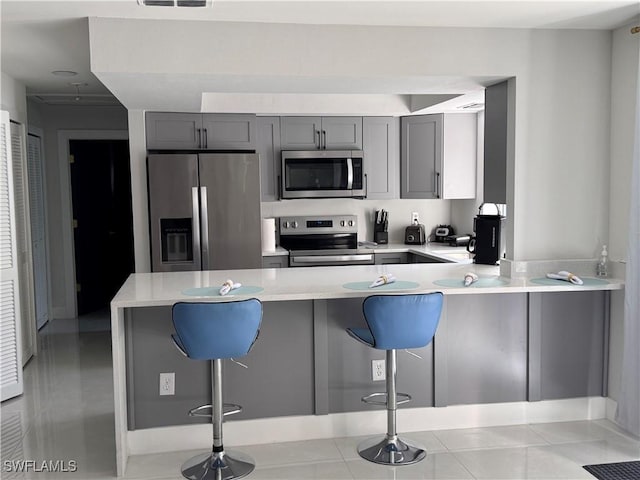 kitchen with a breakfast bar, gray cabinetry, and stainless steel appliances