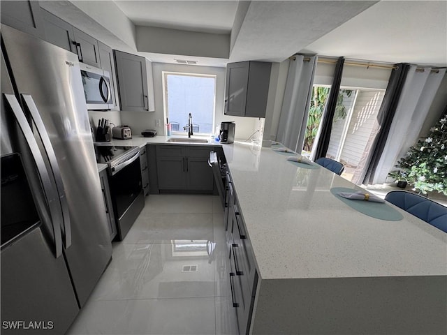 kitchen with a kitchen bar, sink, gray cabinetry, and stainless steel appliances