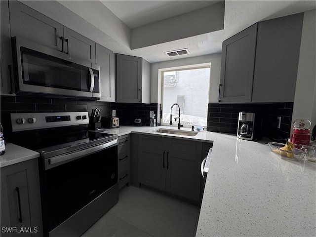 kitchen with gray cabinets, appliances with stainless steel finishes, tasteful backsplash, and sink