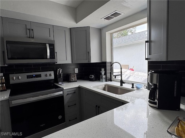 kitchen featuring stainless steel appliances, gray cabinetry, decorative backsplash, light stone countertops, and sink