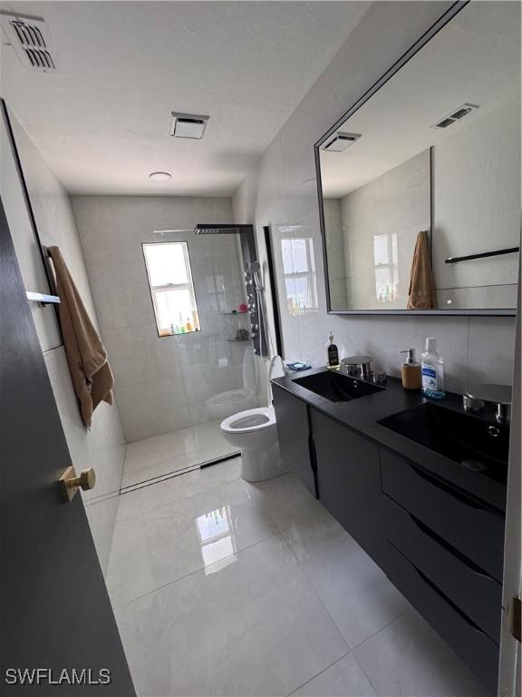 bathroom with vanity, toilet, tile patterned floors, and tiled shower