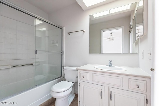 full bathroom with toilet, vanity, combined bath / shower with glass door, wood-type flooring, and a skylight