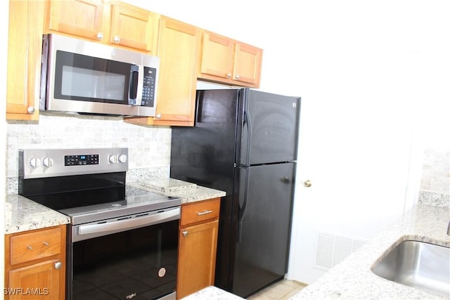 kitchen featuring visible vents, decorative backsplash, light stone countertops, stainless steel appliances, and a sink