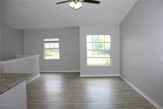 spare room with dark wood-type flooring, a healthy amount of sunlight, baseboards, and a ceiling fan