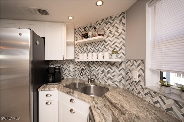 kitchen featuring light stone countertops, stainless steel fridge, sink, and white cabinetry