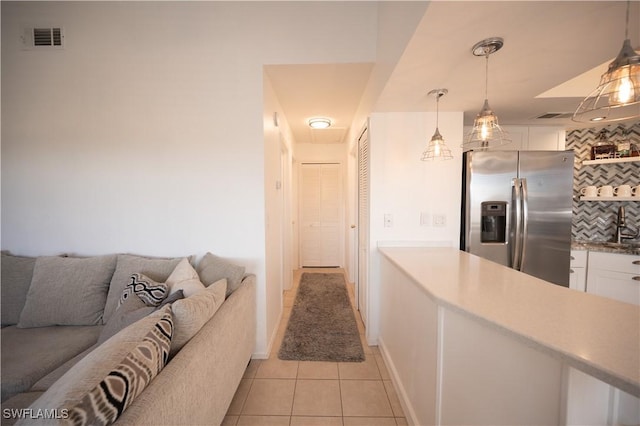 interior space with decorative light fixtures, white cabinets, stainless steel fridge, and light tile patterned floors