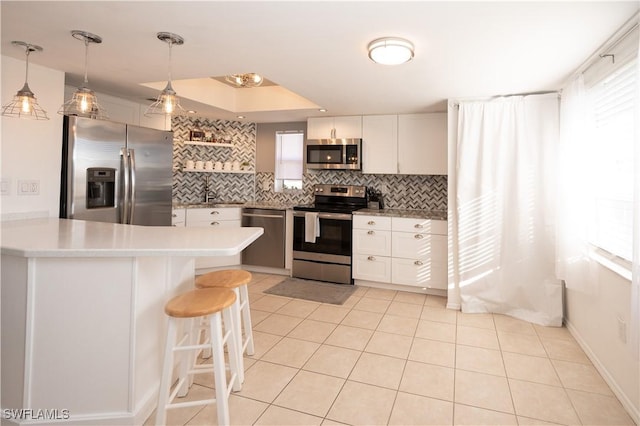 kitchen featuring white cabinetry, kitchen peninsula, appliances with stainless steel finishes, decorative backsplash, and a breakfast bar