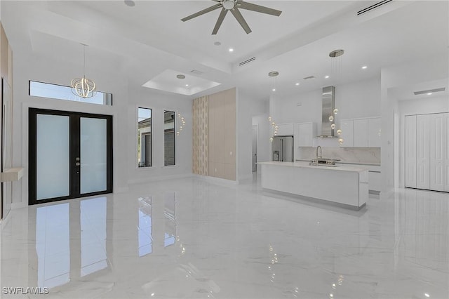 interior space featuring stainless steel fridge, hanging light fixtures, a kitchen island, wall chimney exhaust hood, and white cabinets