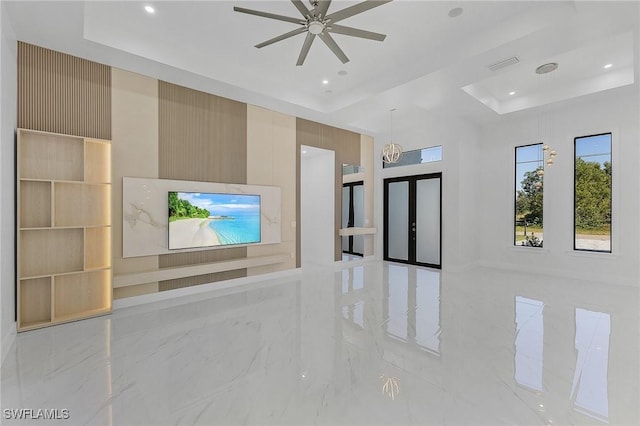 unfurnished living room featuring french doors, built in features, ceiling fan with notable chandelier, and a raised ceiling