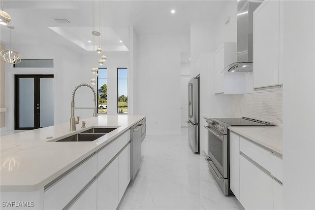 kitchen with hanging light fixtures, white cabinets, appliances with stainless steel finishes, and wall chimney range hood