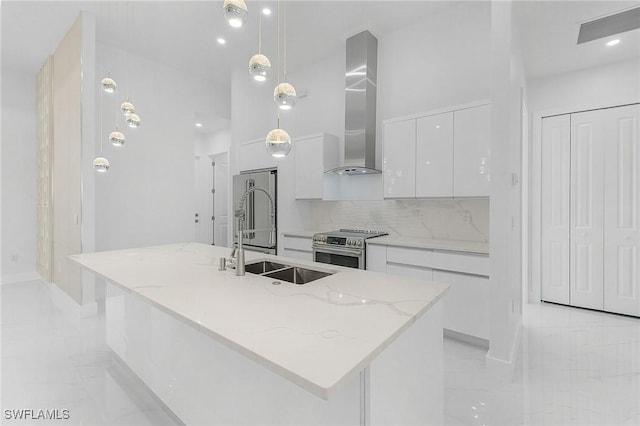 kitchen with decorative light fixtures, wall chimney range hood, stainless steel appliances, and a center island with sink