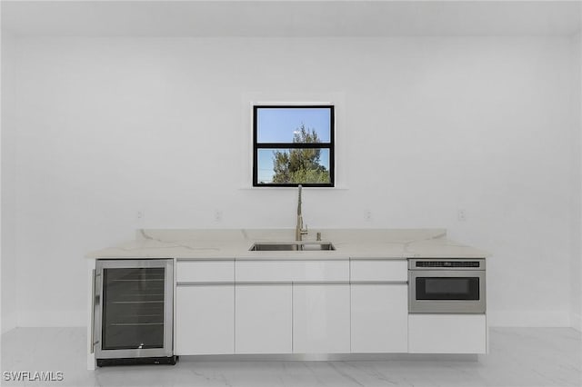 kitchen featuring white cabinetry, wall oven, beverage cooler, light stone countertops, and sink