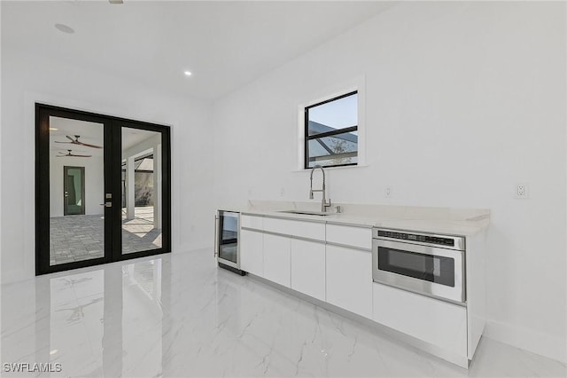 kitchen with white cabinetry, wine cooler, sink, wall oven, and ceiling fan