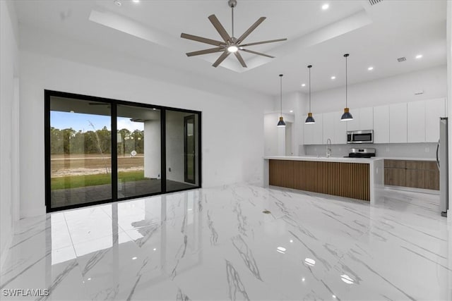 kitchen with a large island with sink, a raised ceiling, sink, white cabinetry, and stainless steel appliances