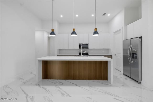 kitchen with white cabinetry, hanging light fixtures, stainless steel appliances, and an island with sink