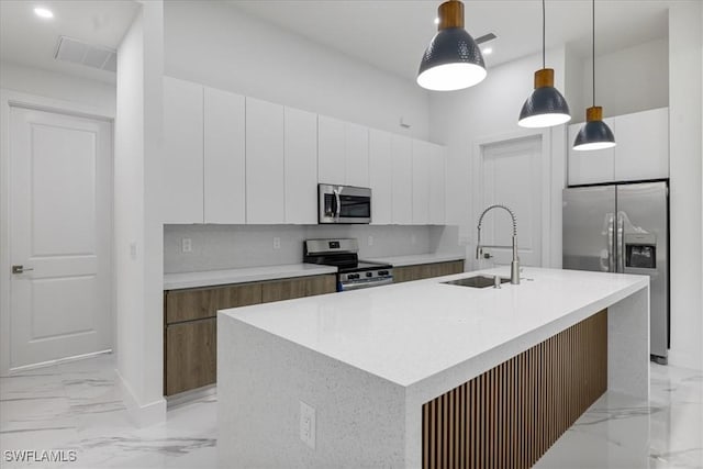 kitchen with decorative light fixtures, white cabinets, appliances with stainless steel finishes, and an island with sink