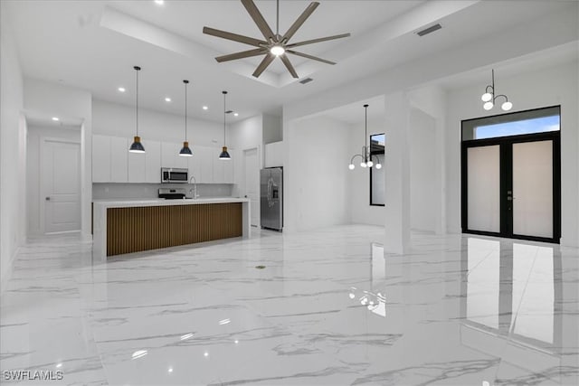 kitchen with decorative light fixtures, a large island with sink, white cabinetry, stainless steel appliances, and ceiling fan with notable chandelier