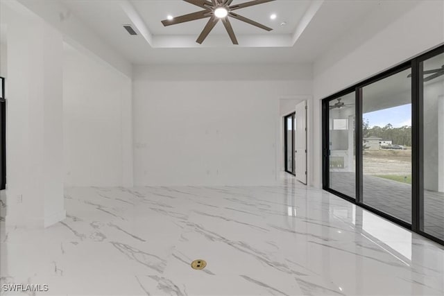 empty room with ceiling fan and a raised ceiling