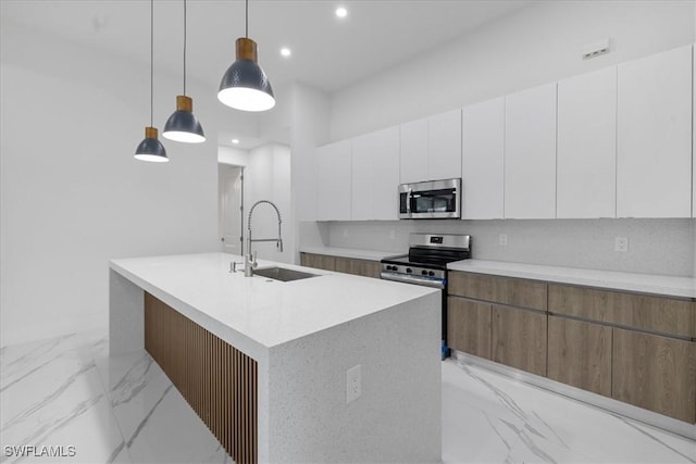 kitchen with an island with sink, stainless steel appliances, hanging light fixtures, white cabinets, and sink