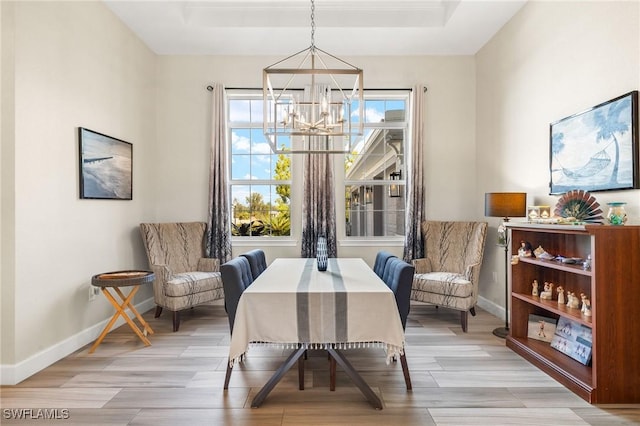 dining space with light wood finished floors, baseboards, a tray ceiling, and a notable chandelier