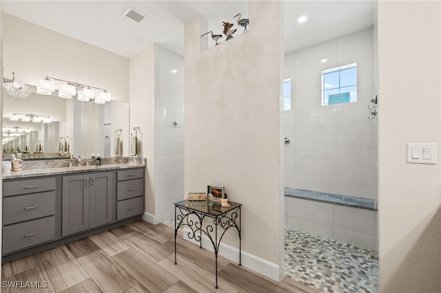 full bathroom with wood finish floors, visible vents, vanity, a walk in shower, and baseboards