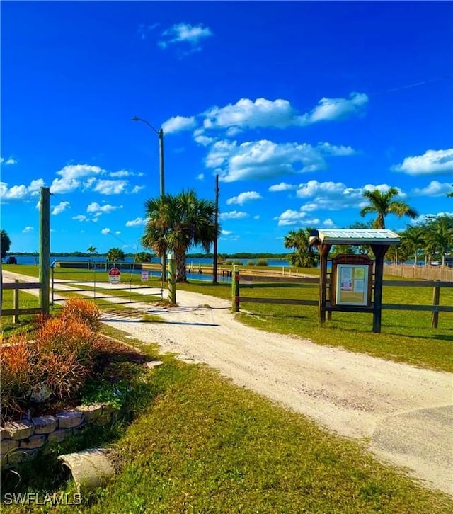 view of home's community with a yard, a water view, driveway, and fence