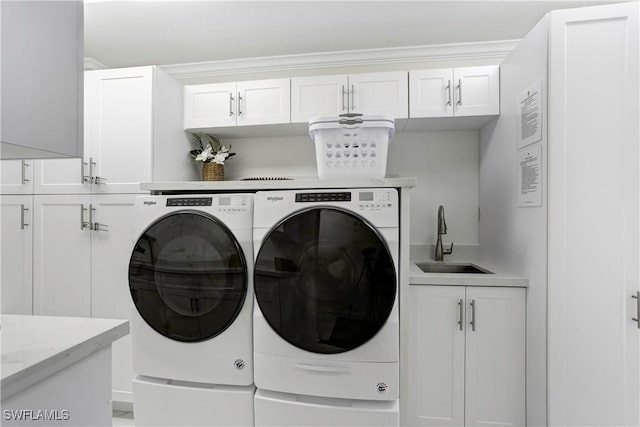 clothes washing area featuring cabinets, sink, and washer and clothes dryer