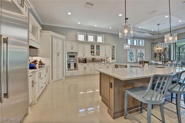 kitchen featuring decorative light fixtures, a spacious island, a breakfast bar, light stone countertops, and stainless steel appliances