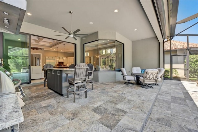 view of patio featuring ceiling fan, glass enclosure, and an outdoor kitchen